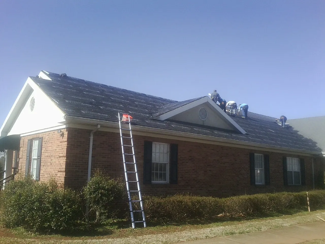 Crew tearing shingles off a brick ranch roof with a ladder set — Emergency Roof Repair work by our crew in Decker