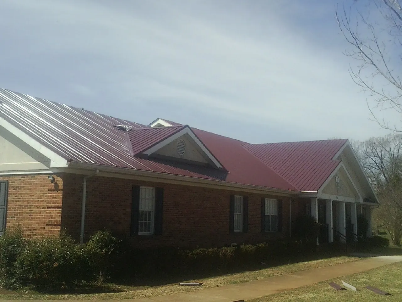 Red metal roof with gabled entries on a long brick building, from a Hail Damage Roof Repair job in Decker